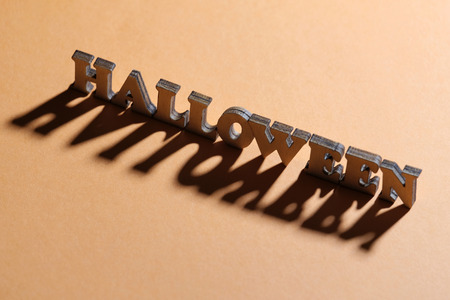 Theme for the holiday of All Saints. HALLOWEEN inscription with a long shadow in the backlight. Words of wooden letters on a beige background.の写真素材