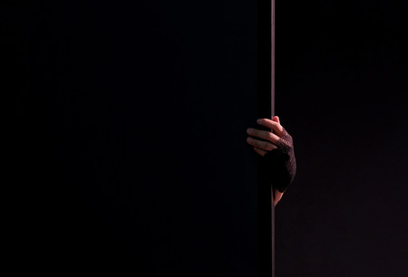 Female hand in black gloves holds edge of wall. Black background. Close-up. Copyspace. Theme for the design of the holiday Halloween. Mysticism, horror and fear.の写真素材