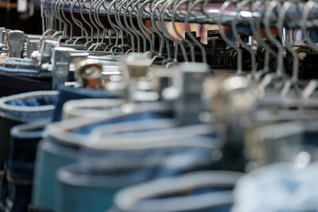 Jeans blue on metal hangers in the clothing store. Blurred background for design shopping and sales. Close-up. Shallow depth of field.の写真素材