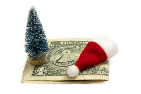 A toy red Santa Claus hat, a Christmas tree souvenir on the one US bill. The concept of the cost of celebrating the New Year or how much it costs to celebrate NY in America.の写真素材