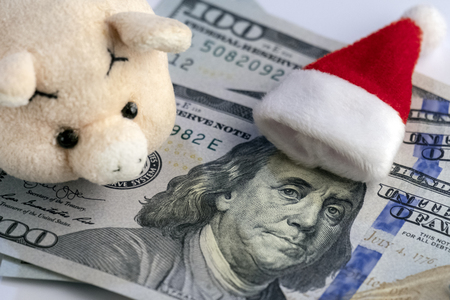 Meet the New Year without financial debts. The Santa Claus hat lies on Franklin's head on one hundred dollars, a pink soft toy pig, and a Christmas tree souvenir. How much money do people spend on New Year's holidaysの写真素材
