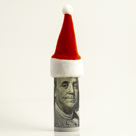 One hundred-dollar bill is rolled up and the red Santa Claus hat at the top. Funny portrait of President Franklin. Financial concept for Christmas decor. New year surprise. White background. Square frame.の写真素材
