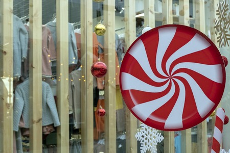 A large circle with a red and white spiral pattern, Christmas balls and a snowflake hang on the background of a shop window with clothes. Abstract New Years decor in the store. The concept of holiday shopping theme.の写真素材