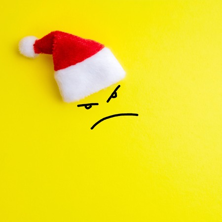 Emotion of evil face expression and red santa claus hat on yellow background. The concept of the New Year and Christmas.. Square drawing. Copy spaceの写真素材