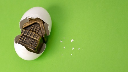 Souvenir toy building in a broken egg on a green background. White eggshell with a golden gift instead of yolk inside. Concept happy birthday new home. Mortgage or loan for housing. Copy space.の写真素材