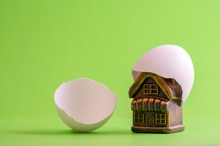 Eggshell on a souvenir house. Toy building and a broken egg on a green background. The concept of newborn housing or housewarming. Copy space.の写真素材