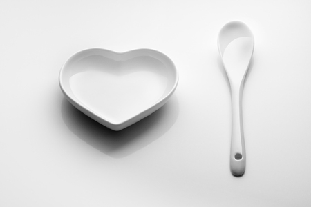 Heart saucer and ceramic spoon on a white background. For design on Valentine's Day, wedding, romantic dinner. Minimalism.の写真素材