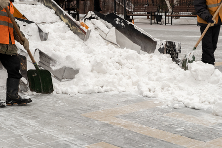 Snow removal on the streets. People and cars. Abundance of snow. Winter. Close-up of a snowplow and road workers with shovels.の写真素材