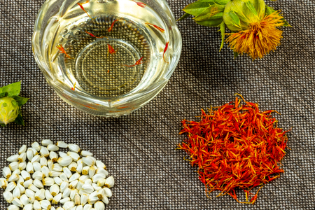 Safflower. Oil, seeds, bud, flower, red inflorescences of wild saffron. Close-up, Gray woven background. Ingredients for health, cosmetology and paintの写真素材