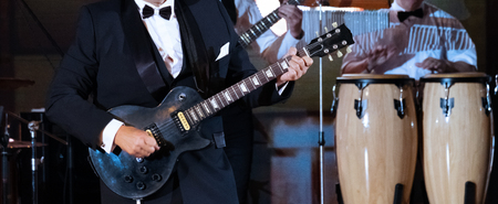 Jazz band performance. An abstract man in a strict suit plays the guitar on the scene in the foreground. Close-up. Drums in the background. Concept for the design of a musical theme.の写真素材