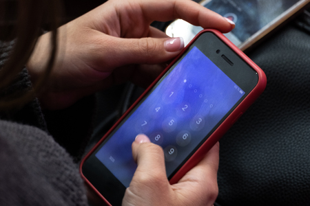 Close-up. Red mobile phone in female hands. A girl is calling or dialing numbers pin code on a blue screen smartphone similar to an iPhone.の写真素材