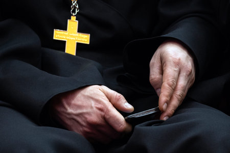Mobile phone in the hands of an Orthodox priest. Religious man with a smartphone. Black cassock and gold cross. Communication with god. Religion and modern culture.の写真素材