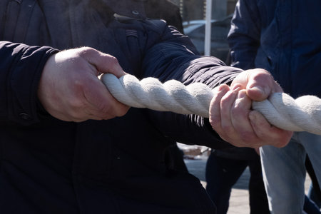 Tug of war. Male hands holding a rope. Folk games and fun. Autumn or spring. Close-up.