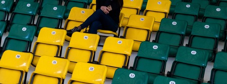 A girl with a mobile phone in her hand on a seat. The auditorium in the sports complex with green and yellow plastic seats. Lonely sports spectator. Blank for website header or web banner.の写真素材