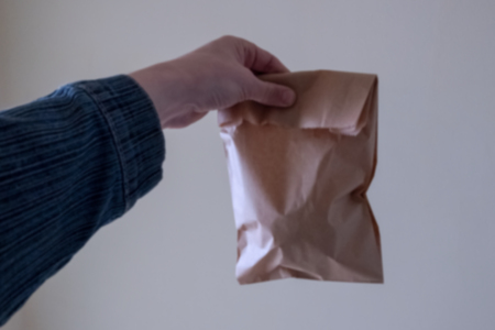 Blurred. Man holding a brown paper bag with contents in his hand. Background for the design concept of product delivery in environmentally friendly packaging.の写真素材