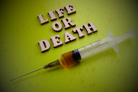 Inscription Life or death from wooden letters next to a syringe on a green background. Medical concept. Vignettingの写真素材