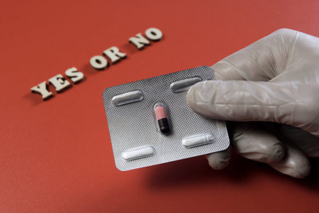 The inscription YES OR NO from wooden letters. Male hand in white glove holds a medicinal pill. The...