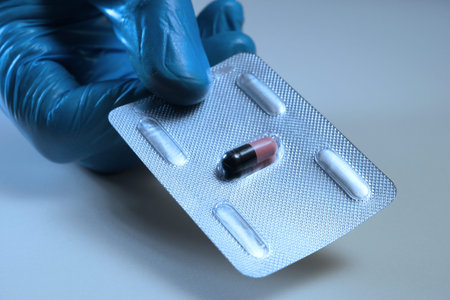 A pill for a terrible disease. A hand in a blue glove holds a medicine capsule, drawing it into the...