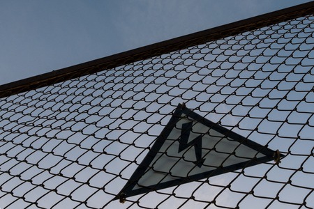 Silhouette. Warning triangular sign with lightning symbol on the fence. Life threatening. No entry. High voltage concept.の写真素材