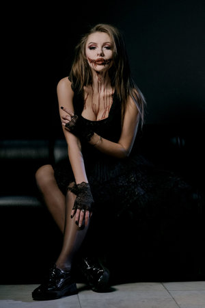 Halloween makeup, horror party costume. Sexy girl with big breasts in black clothes in the form of a...