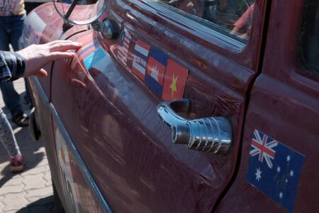 Kazakhstan, Kostanay, 2019-06-20, The 7th Peking to Paris Rally Motor Challenge. Close-up. The hand of an elderly person touches the door of a retro car with flags of different countries pasted on it.のeditorial素材