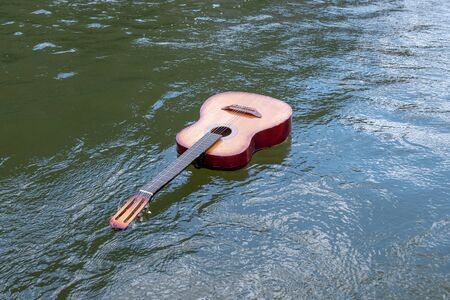 Music does not sink. An acoustic guitar floats in a river, lake or other body of water. Copy space. The concept of shipwreck, flood, tragedy of musicians in nature.の写真素材