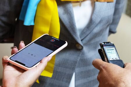 Recording an interview. Reporters and speaker. Noise and film grain.Close-up. A male hand with a voice recorder and a female hand with a phone. Selective focus.の写真素材