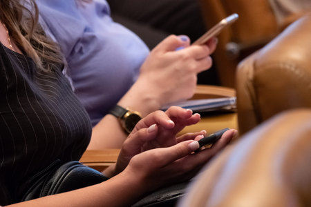 Blurred background, selective focus. Abstract girls sit in a conference room and hold mobile phones...