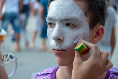 Make-up artist's hand puts white paint on the face of a teenager. Close-up. Street makeup for a...