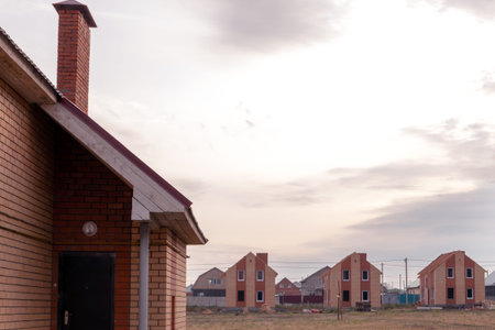 Construction of typical houses of red and yellow bricks. Part of the roof and the door in the foreground. Image for articles on the topic new available under the state program or bank mortgage lending. Copy space in the sky.の写真素材