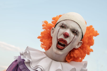 Portrait of a guy in the image of a clown with sharp teeth on a background of blue sky. Carnival...