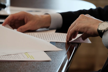 Men's hands with a wristwatch turn over documents on the table. An official, banker or boss reads an...