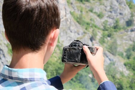 A molten charred SLR camera in the hands of a teenager. How to take pictures of a burned-out device. The tropical heat ruined the camera. The concept of camera repair after extreme travel.の写真素材