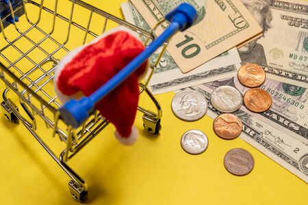 A shopping souvenir stroller for products with a Santa Claus hat costs about US dollars and cents. Americans spend on Christmas and New Year holidays. Yellow background. Concept. Online and offline shopping.の写真素材