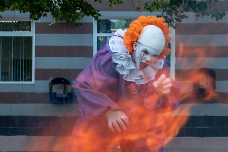 Clown with sharp teeth on fire on a urban background with payphones. The concept of fear and horror. Halloween or cosplay for All Saints Day.の写真素材
