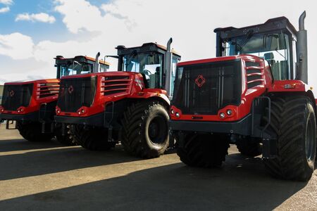 Kostanay, Kazakhstan, 2019-10-23, Three red tractor of the Russian brand Kirovets on the area of the factory territory. Long shadows from cars due to the bright sun.のeditorial素材
