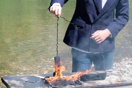 A laptop and a phone burned out on an office desk near the river. The male hand of a freelancer, manager or businessman holds the wire of the telephone receiver on fire. The concept of hated work or insurance case. Loss of digital data or the intentional destruction of electrical appliances. Technical Support Hotline.の写真素材
