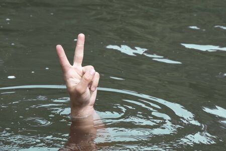 Male hand in the water with hand raised up. A person drowns in a river or lake and shows a symbol of victory and freedom. Winner concept in spite of problems. Copy space.の写真素材