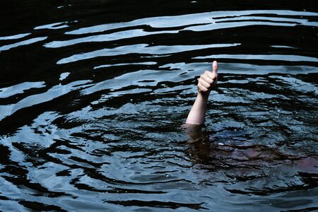 A male hand with a raised finger sticks out of an oil-like fluid. A man is drowning in black water. The concept of excellent quality or low price of petroleum products. Copy space.の写真素材
