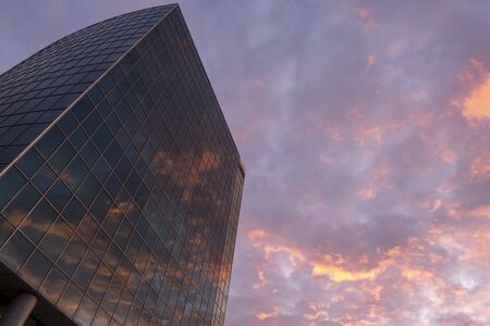 Modern glass high rise business building with reflected sunset in it. Evening red clouds. Copy space. Wallpaper. Great city view.の写真素材