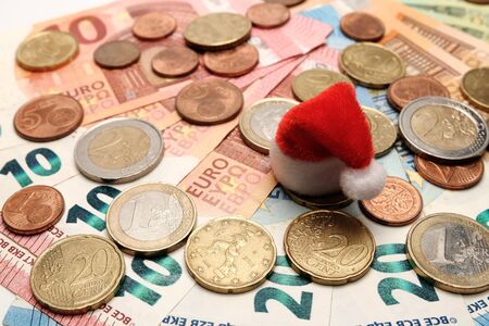 Red santa claus hat on a background of euro coins and banknotes. The concept of New Year and Christmas spending and gifts. Background of european money.の写真素材