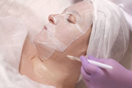 Anti-aging skin treatment. Cosmetology. The mask on the woman's face. The girl in the beauty salon at the reception of a cosmetologist.の写真素材