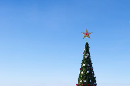 Christmas tree. The crown of a big New Year tree with a star and toys against a blue cloudless sky. Festive winter mood and holiday decoration. Copy space.の写真素材