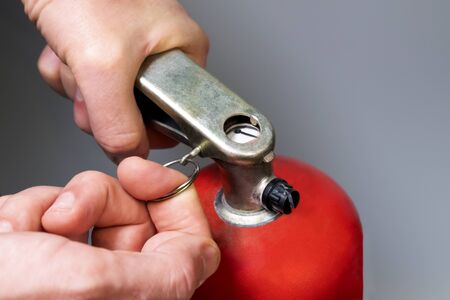 Male finger pulls out a pin. A man pulls out a safety ring from a red fire extinguisher. Fire fighting regulations. Close-up. Emergency Prevention. Shallow depth of field. Selective focus.の写真素材