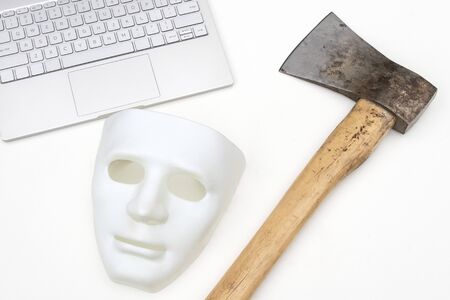 Mask, computer and ax on a white background. Close-up. Conflict criminal concept of cyber attack or defense against hackers.の写真素材