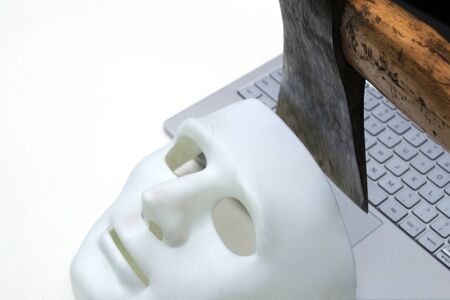 The ax symbolically cuts off the mask of an anonymous hacker from the laptop keyboard. We know how to protect data on your computer - advertising anti-phishing programs. The concept of cyber hacking and protection against online attacks. Close-up.の写真素材