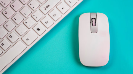 A wireless mouse lies next to a white computer keyboard. Close-up. Blue background. The concept of the office manager or computer salon selling peripheral devices.の写真素材