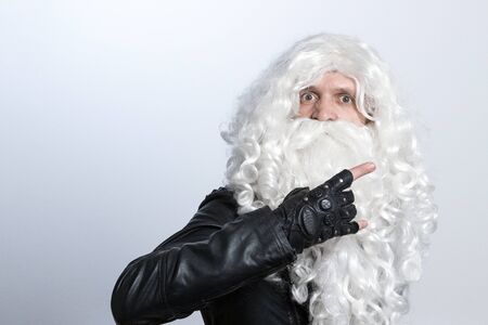 A tough guy in a white wig and a beard like Santa Claus making an heavy-metal gesture and staring at camera. Copy spase. Music rock Christmas concept.の写真素材