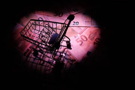 Silhouette of a shopping trolley in a bright light spot in the shape of a heart on euro banknotes. Discount night at a European store. Concept for valentines day, wedding and family sales.の写真素材