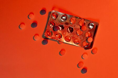 A sense of danger. Open blister and scattered tablets in red light. The concept of medicine, overdose, addiction, suicide, ambulance. Toned background. Copy space.の写真素材